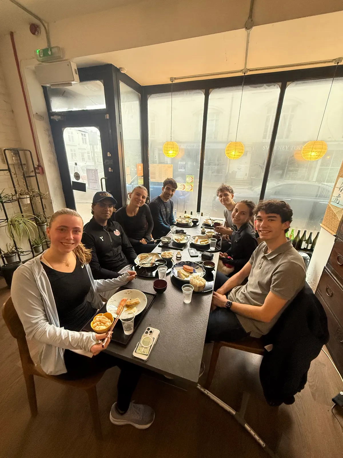 Eight people round a table of food, smiling at the camera