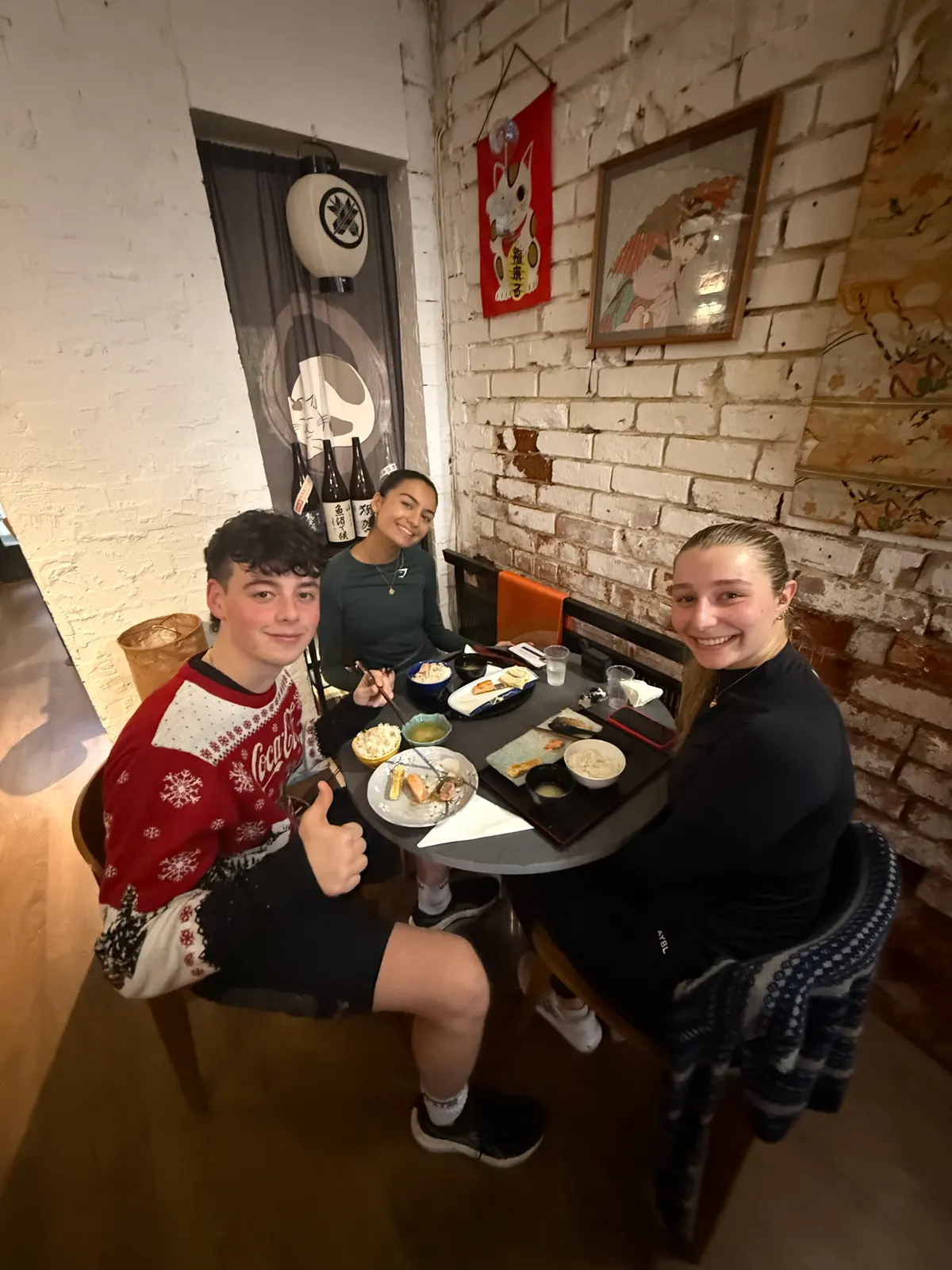 Three people at a small table, one in a Christmas jumper giving a thumbs up