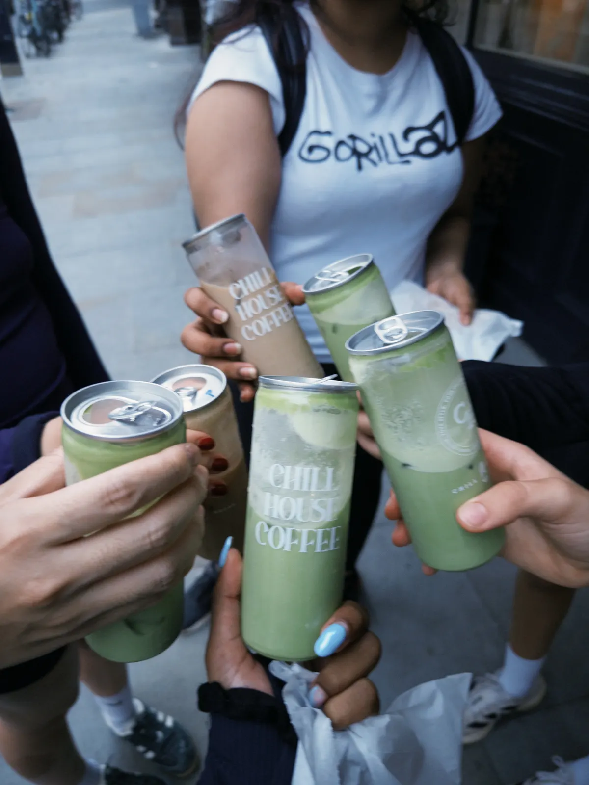 Four hands raising cans of iced coffee and matcha together