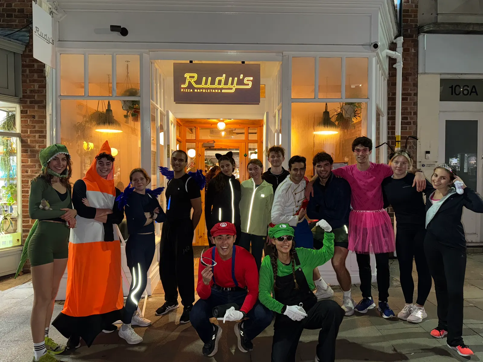 A group of runners in Halloween costumes outside a lit shopfront at night