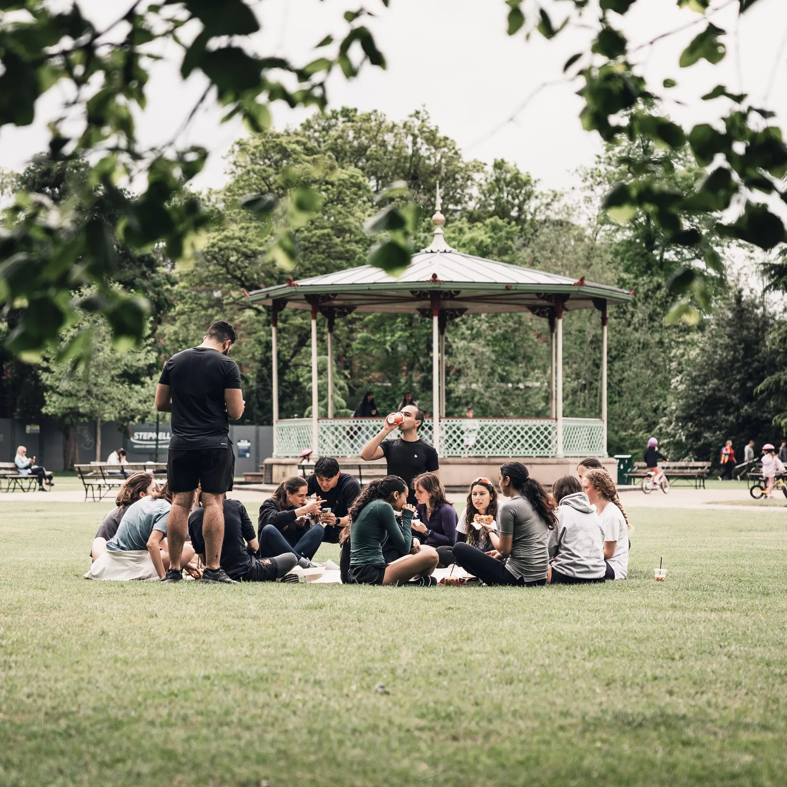 People sitting in a circle on the grass in front of a bandstand